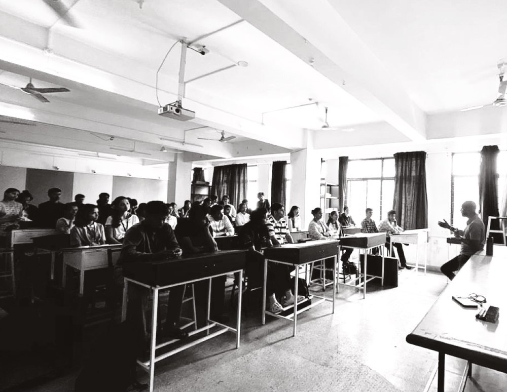 Black and white photo of me speaking to a classroom of architecture students seated at desks