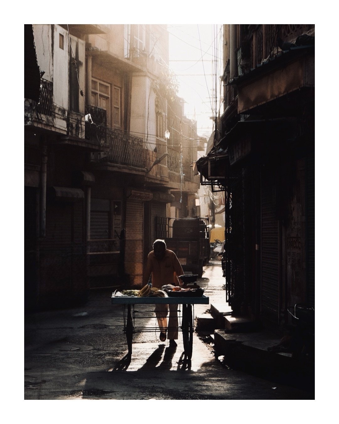Photo of a fruit vendor pushing his cart down a narrow lane in low morning light